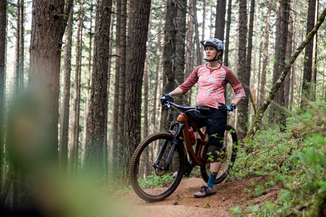 A young, pregnant woman on a mountain bike on a trail in the forest of Oregon.
