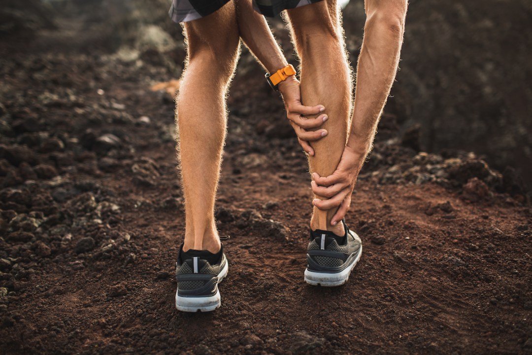 Man holding an injured calf muscle while on a run