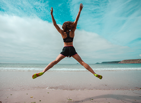 Athletic woman leaping in a star shape on a beach facing towards the sea