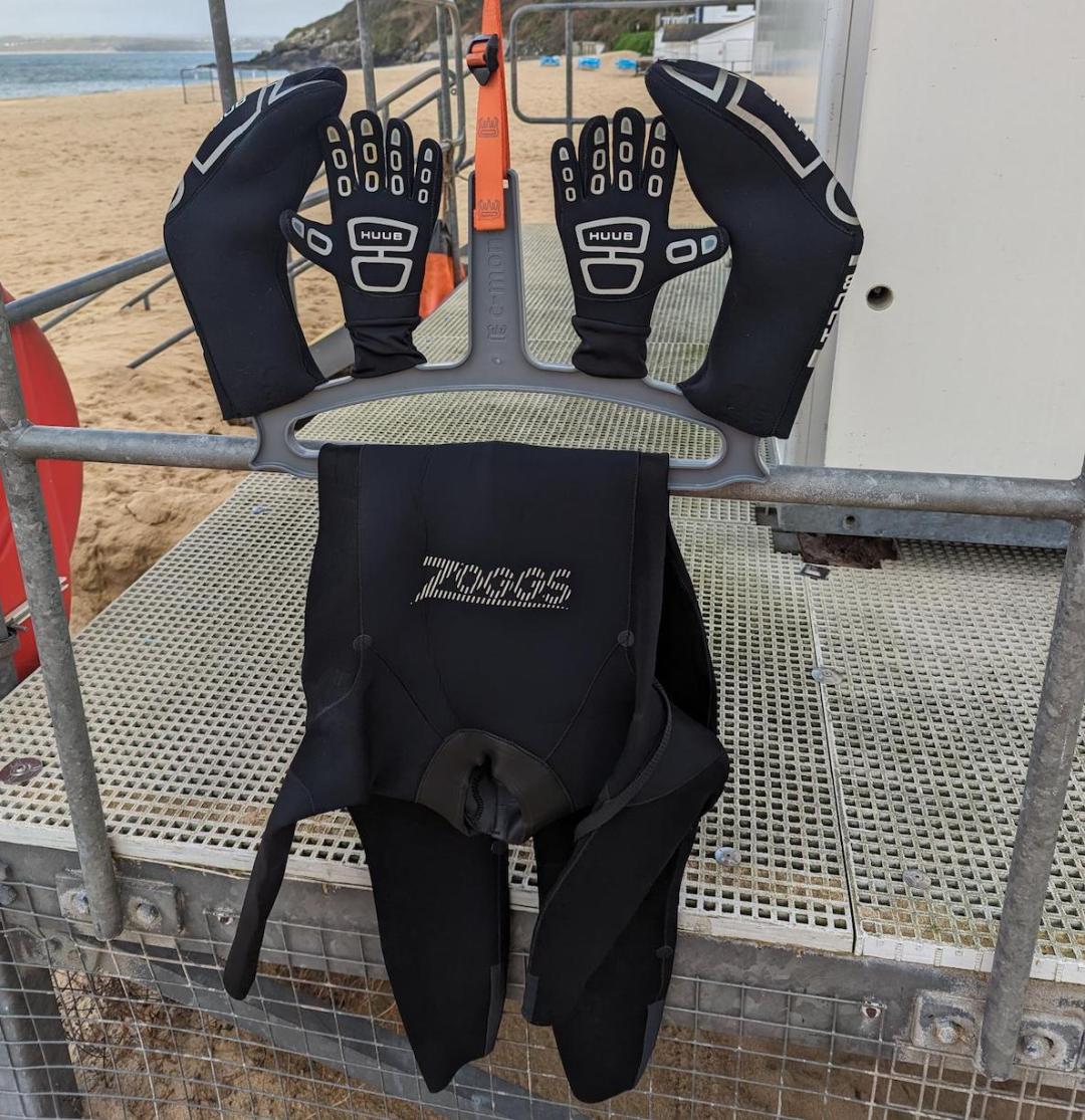 A wetsuit on a wetsuit hanger with neoprene accessories drying out