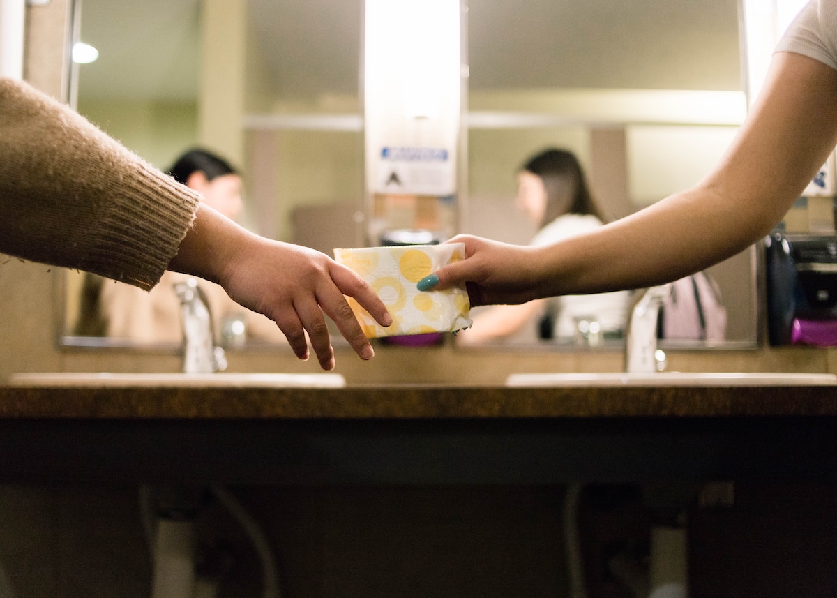 Women passing sanitary products in a bathroom 