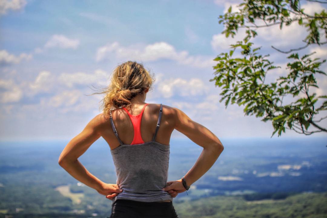 woman starnds iwth hands on hips at top of mountain
