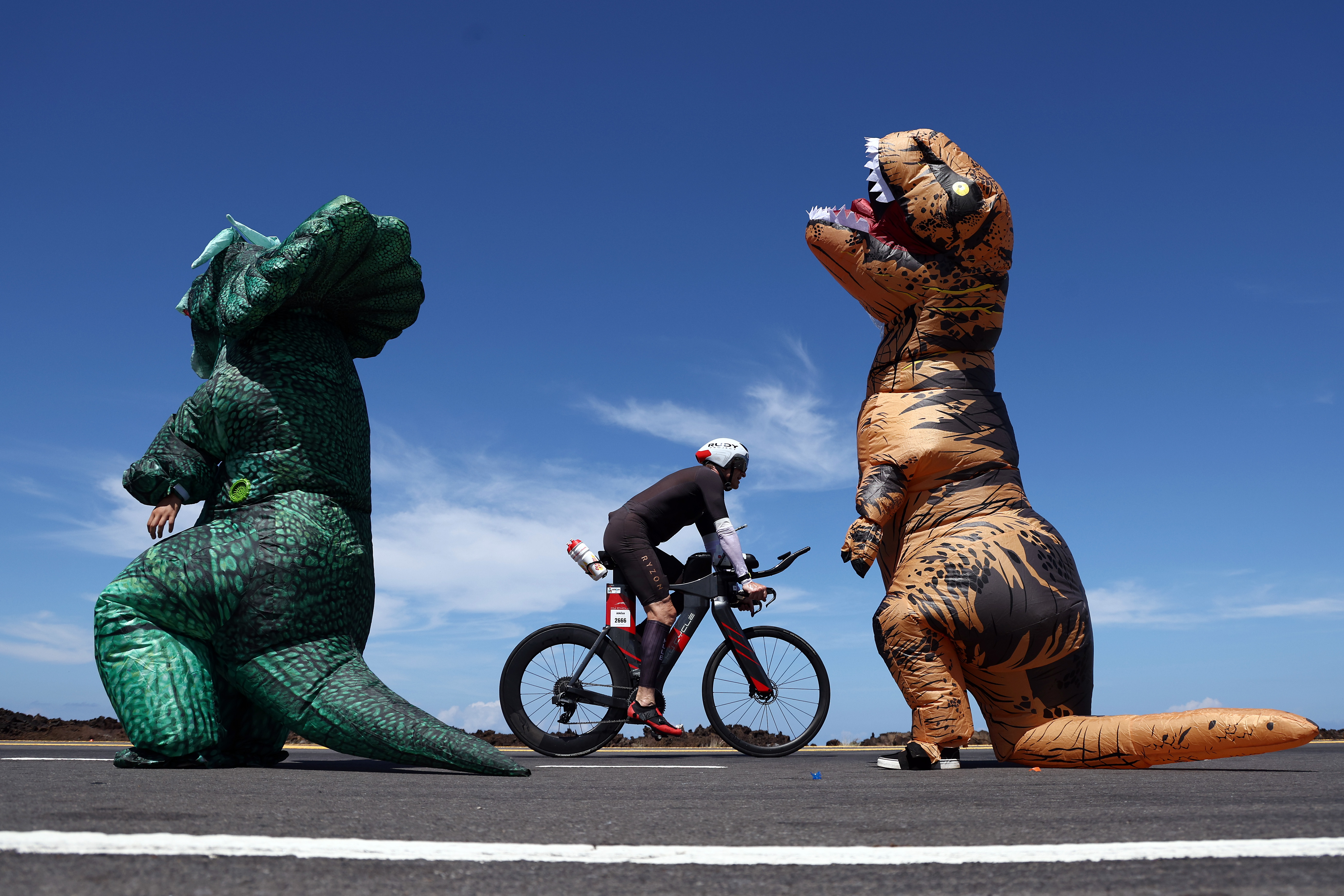 two fans dressed as dinosaurs cheer on a cyclist during the kona race