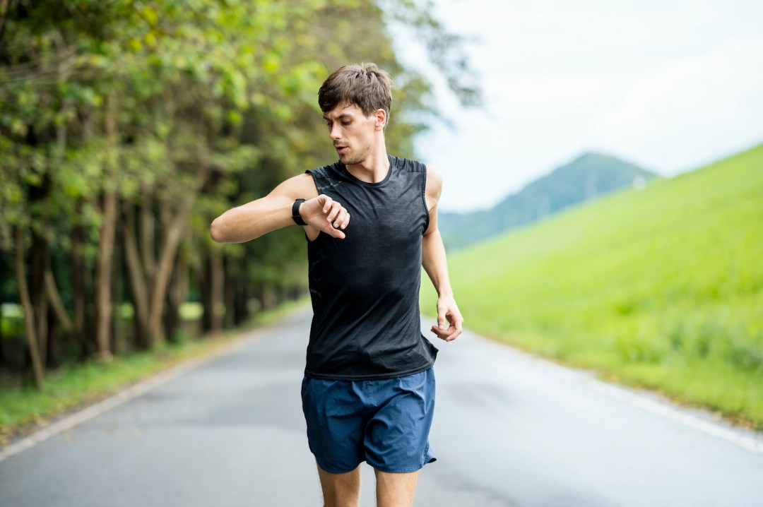 A male runner using wearable run tracking technology while jogging on the street