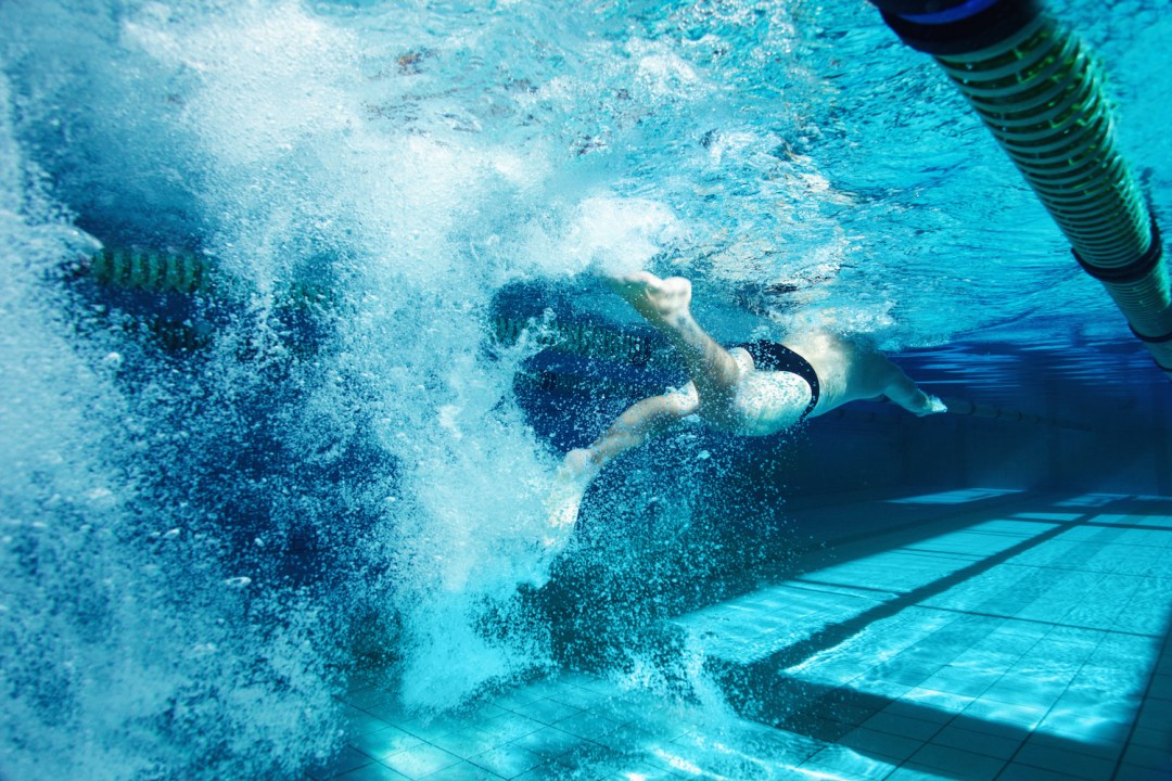 Rearview of a young male competitor swimming freestyle in a pool, kicking underwater