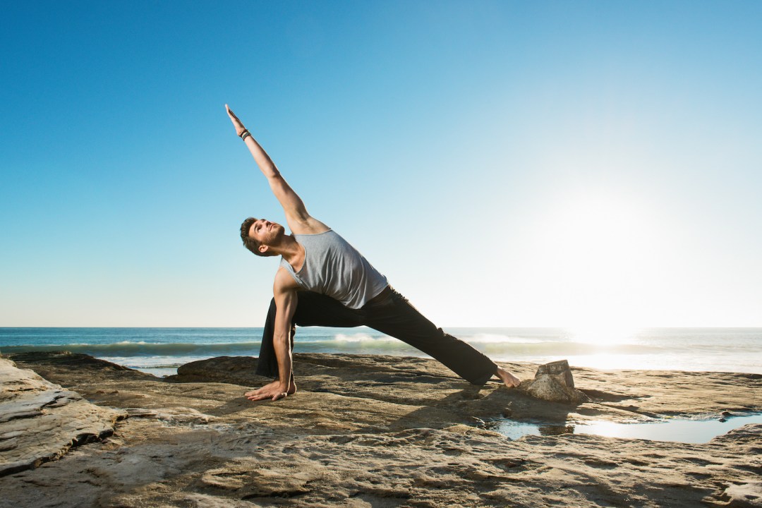 Man doing yoga on a beach with sunrise behind him