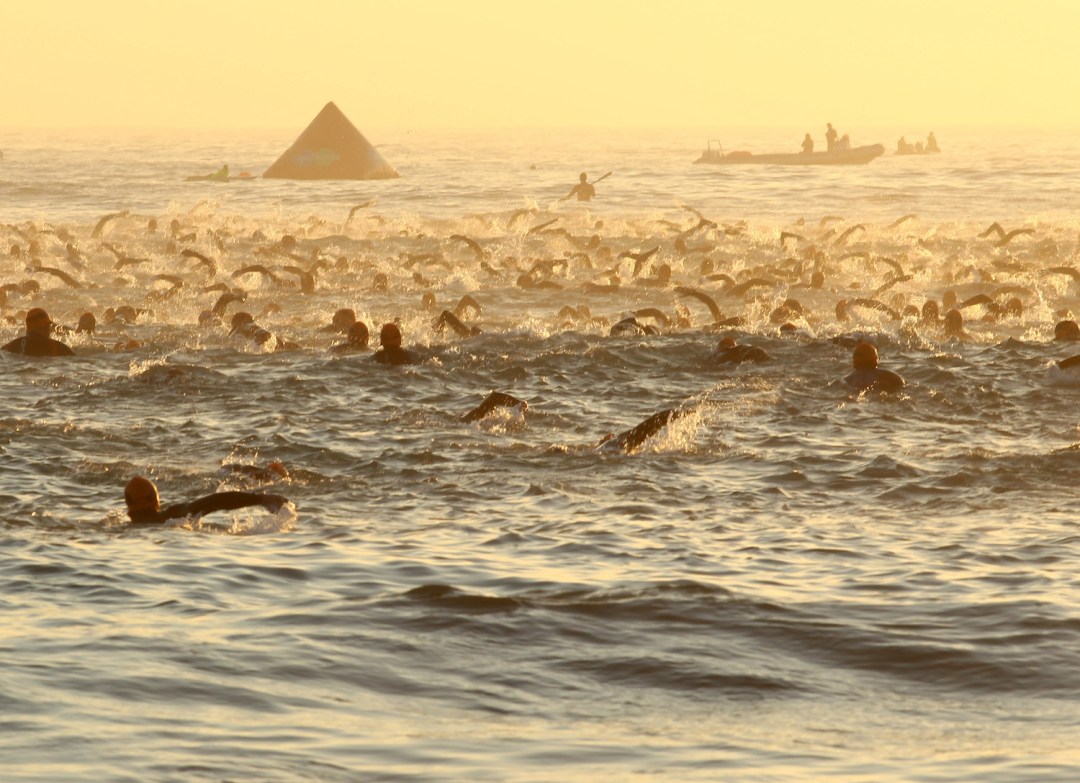 Competitors at Ironman South Africa swimming at sunrise