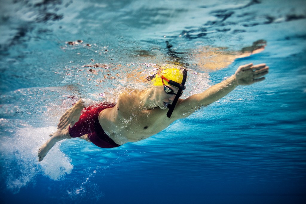 Underwater shot of young man practising front crawl in a swimming pool while wearing a snorkel