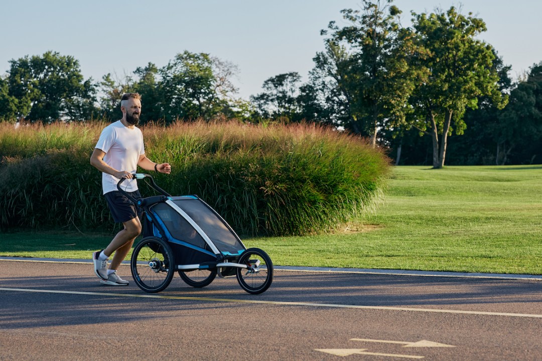 Young father with his kid in a jogging stroller during jogging in a public park