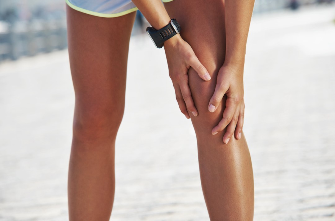A young female runner holding onto her knee as if she is in pain