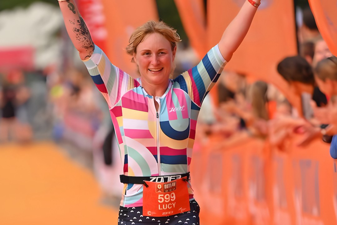 Lucy John runs down the finish line of the 2021 Outlaw Triathlon with arms aloft