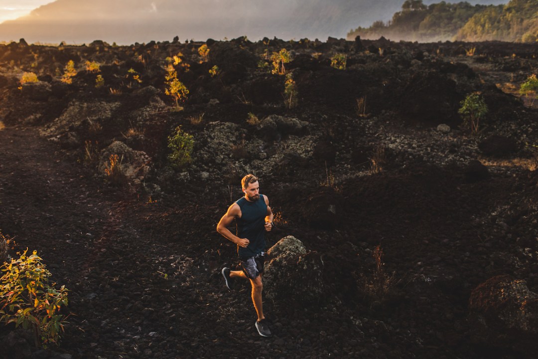 Young male athlete trail running in mountains at sunrise over volcanic rocks
