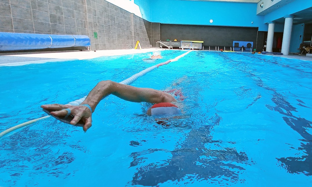 Arm with hand paddle for swimming emerging from water, low angle view