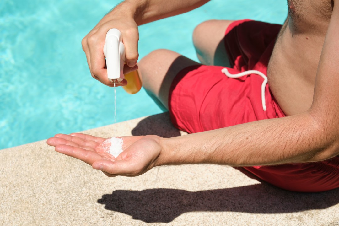 Unrecognisable young man applying sunscreen sitting at the edge of the swimming pool