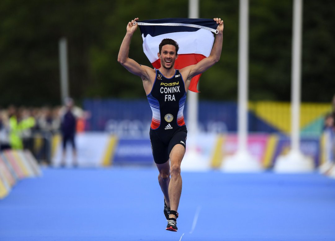 Frenchman Dorian Coninx runs down the blue carpet holding the French flag aloft, on his way to winning the 2018 European Championship Mixed Relay Triathlon in Glasgow, Scotland