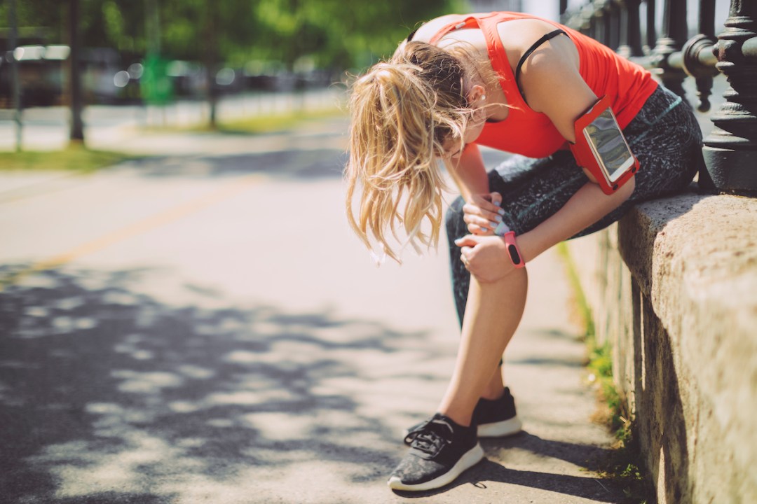 Female runner sits on side of path holding her knee in pain