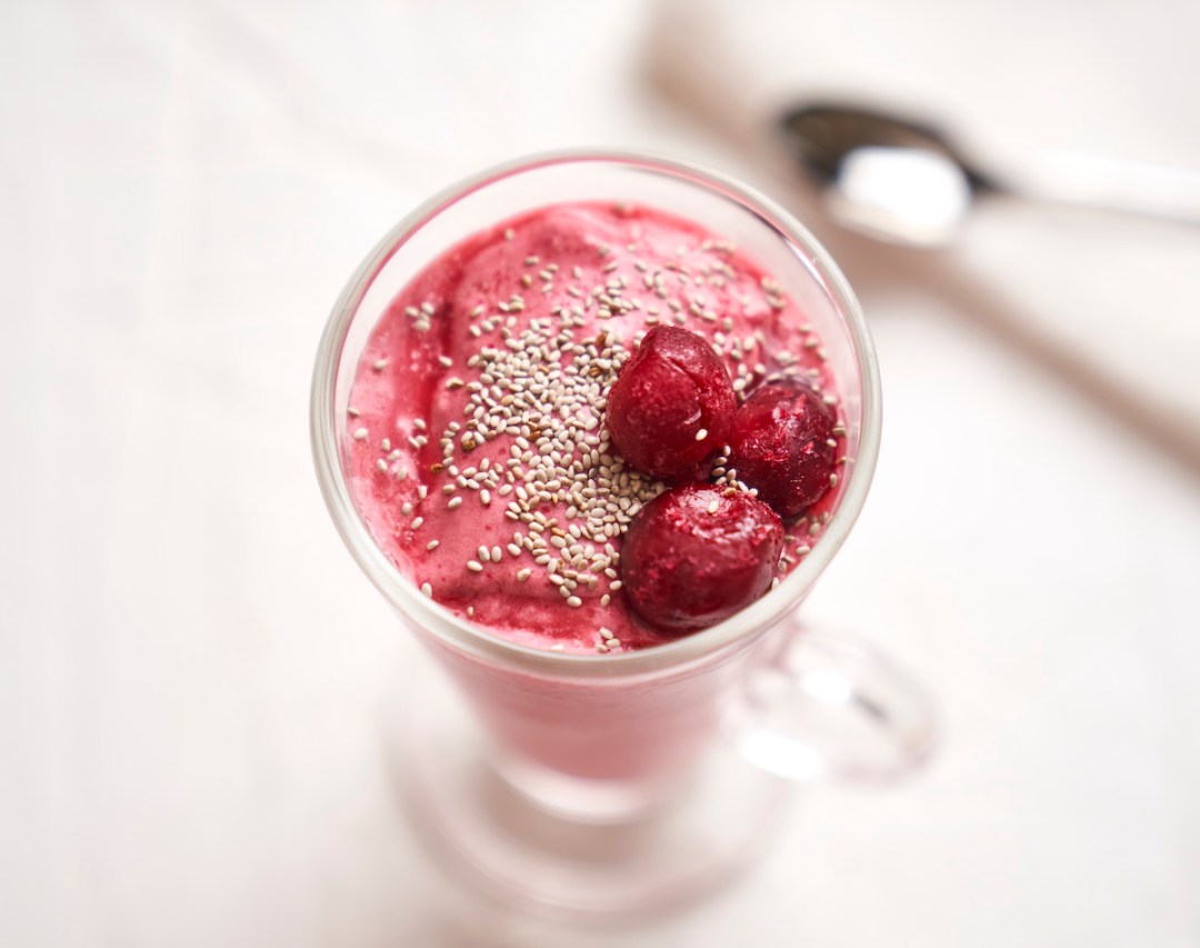 Overhead view of the top of a sour cherry recovery smoothie in a chilled glass, with three cherries and chia seeds on top