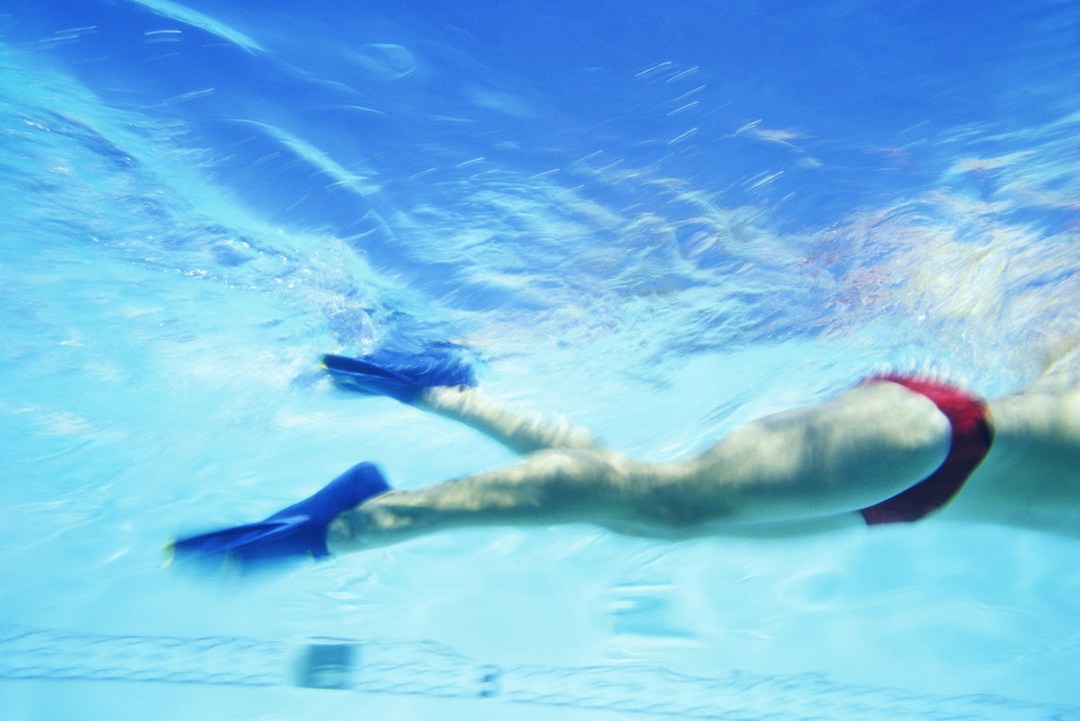 Side-on underwater view of male swimmer's legs wearing fins on each foot