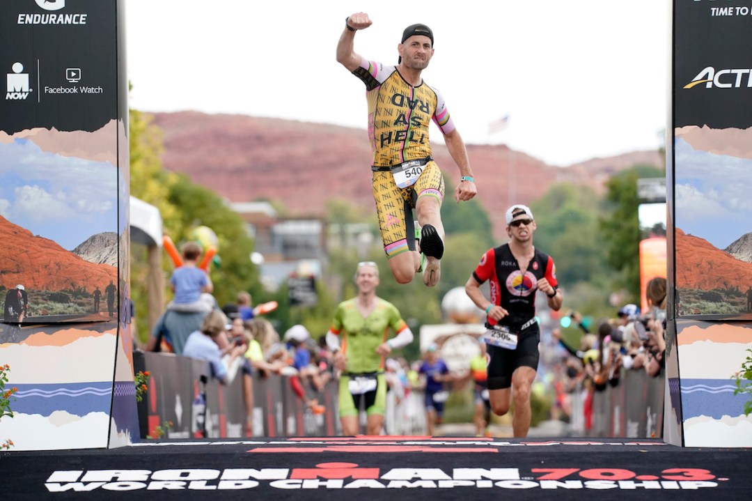 A male triathlete leaps for joy at finishing the 2021 Ironman 70.3 World Championship in St George, Utah