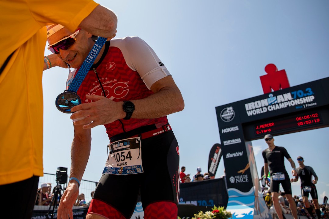 Male athlete collects his finisher's medal from a volunteer at the 2019 Ironman 70.3 World Champs in Nice, France. The finisher's gantry is to the right of the image.