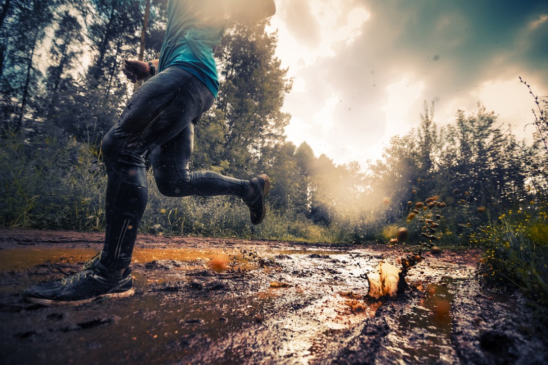 Trail-running athlete moving through the dirty puddle in the rural road