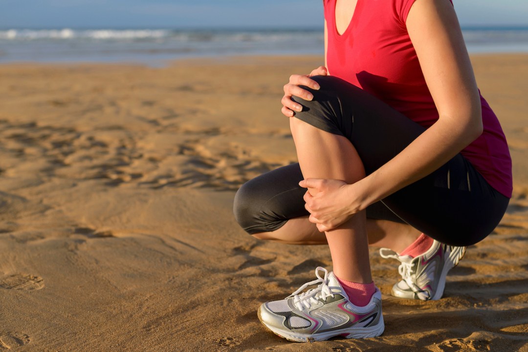 Female runner clutching her shin because of a running injury and inflammation while training on a beach