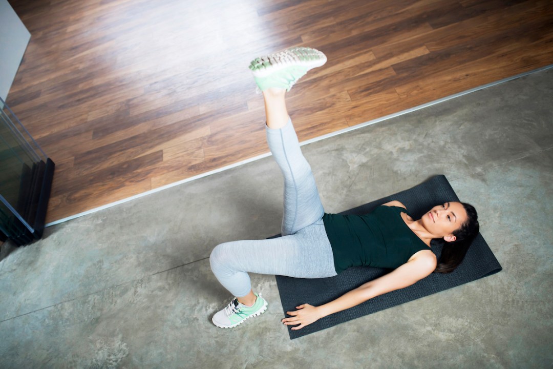 Young woman lying on an exercise mat doing single-leg hip lifts at home