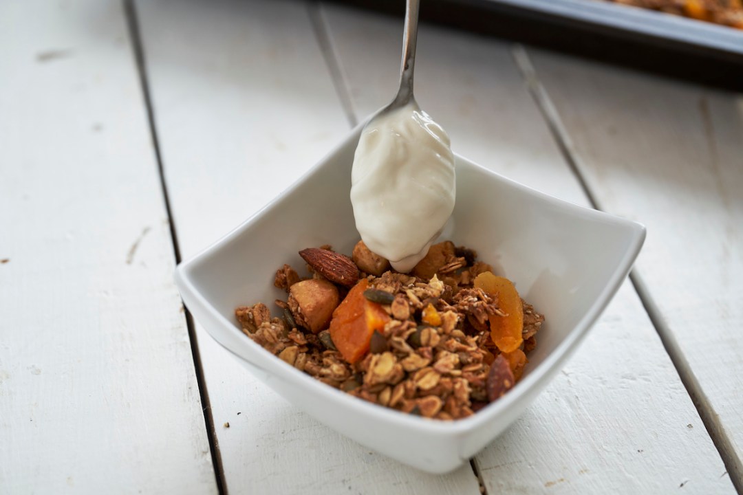 Close up of spoon holding yoghurt over a bowl of granola