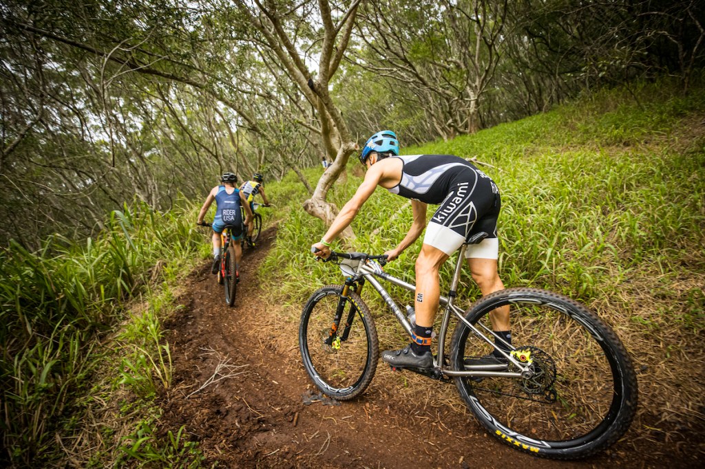 Three male cyclists cycling through wooded area on mountain bikes for an Xterra race