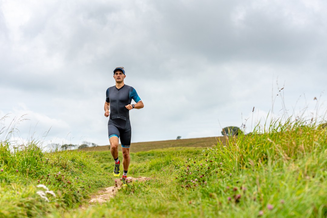 Male triathlete in tri-suit running on a path through a field