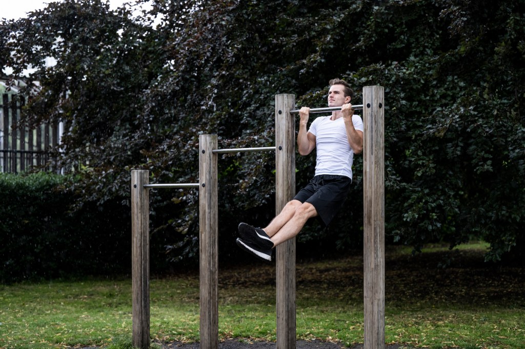 Three-quarter front view of Caucasian man in white t-shirt, black shorts and shoes, strengthening upper back, arm, and abdominal muscles during weekend workout.