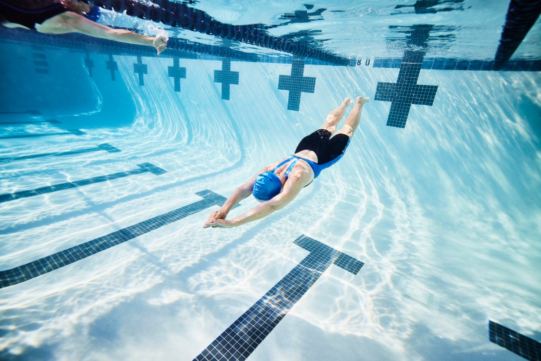 Wide shot underwater view of senior female athlete pushing off wall during workout in pool