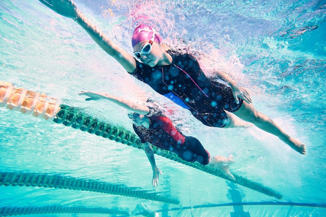 Two swimmers side by side swimming in a pool, shot from underneath in the water