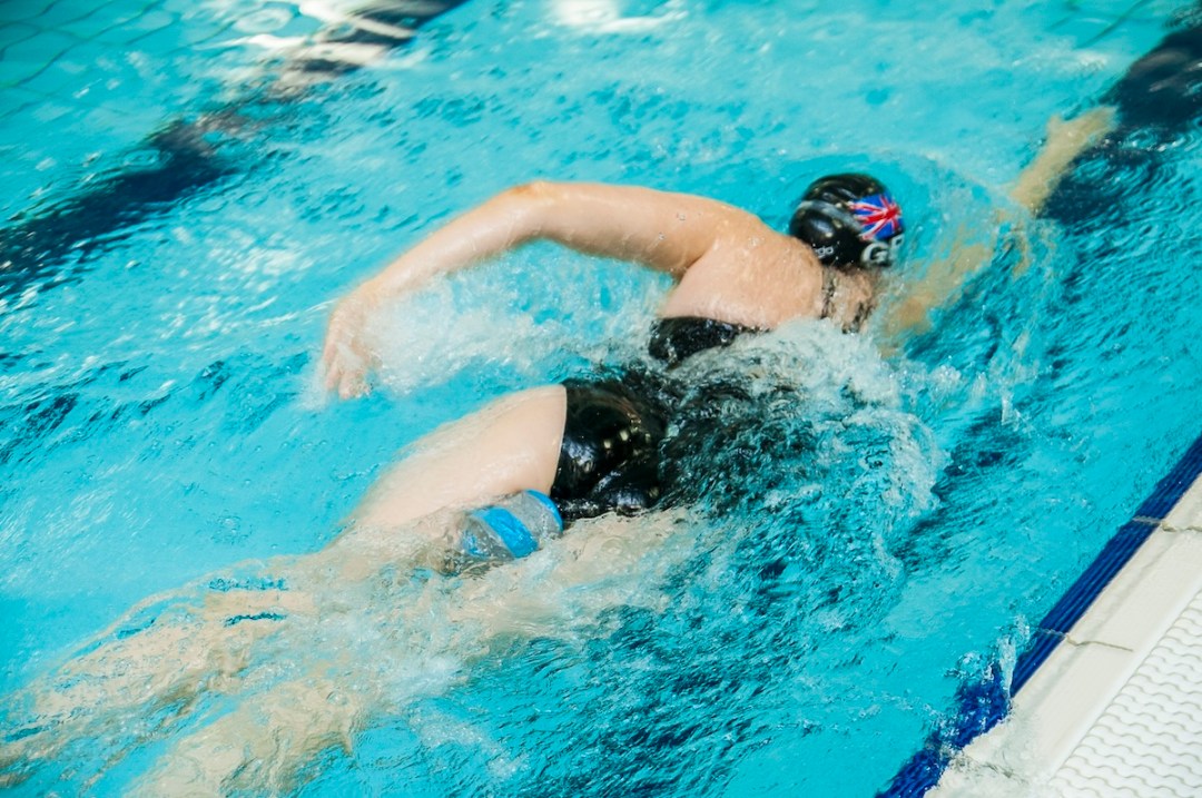 Female swimmer swim training in a pool lane, shot from behind