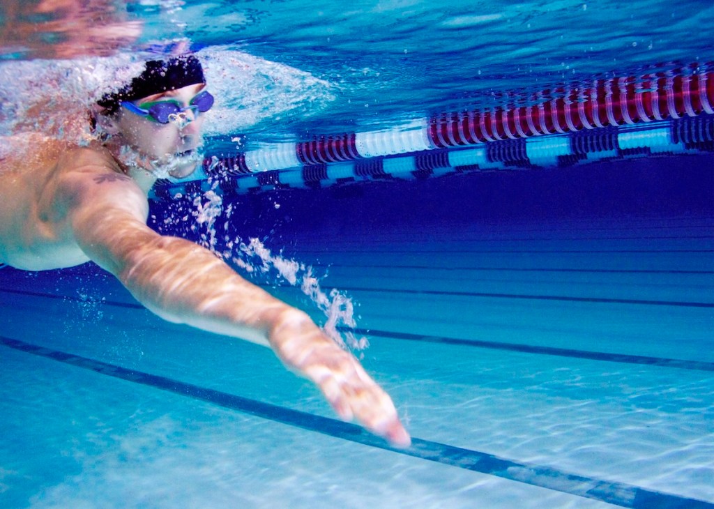 Front shot of swimmer swimming with arms outstretched and goggles on under water