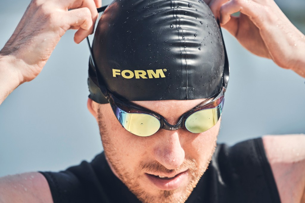 Man adjusting the straps while wearing a pair of Roka R1 swimming goggles