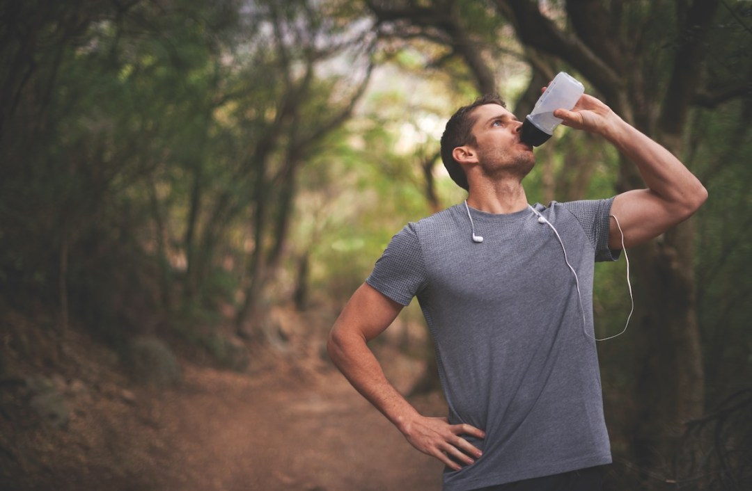 Cropped shot of a young sportsman drinking water while running in the forest