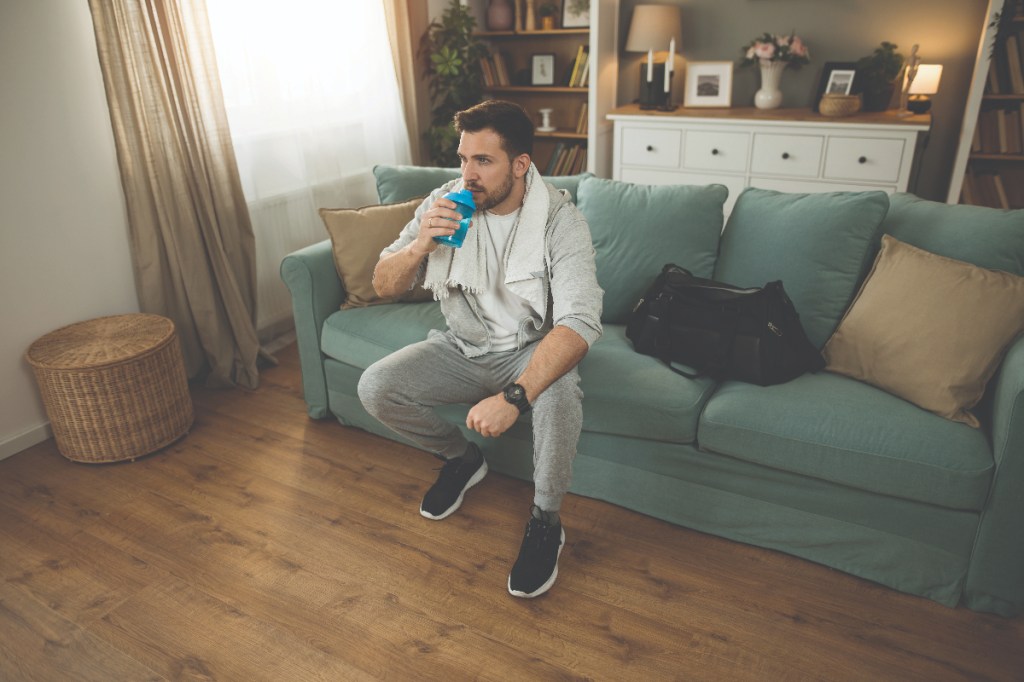 Man sipping drink wearing sports gear on sofa