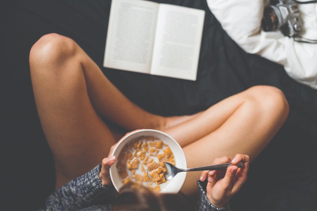 Person eating bowl of cereal reading book