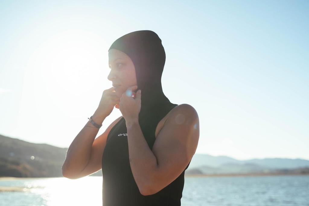 Woman standing by the sea adjusting a neoprene swim vest with hood