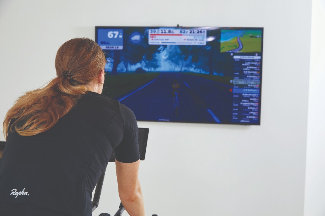 Shot looking over woman's shoulder on to TV showing Zwift ride