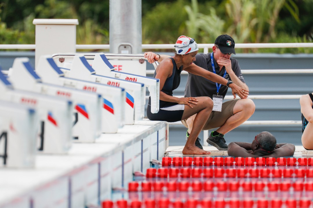 Man squatting beside swimmers by pool